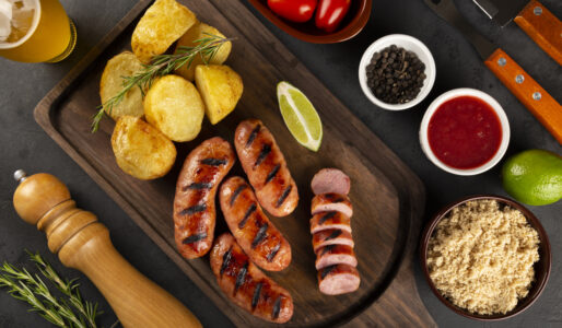 Linguiças grelhadas aceboladas servidas com batatas rústicas em uma tábua de madeira, representando um prato principal completo.